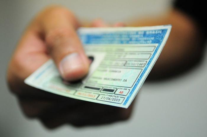 Fotografia de uma mão segurando uma carteira nacional de habilitação. Os dados pessoais na CNH estão embaçados.