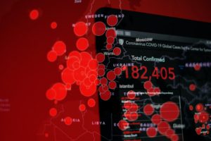 Fotografia em tons de vermelho e preto mostrando monitor de computador, que retrata focos de contágio relacionados à pandemia do COVID-19.