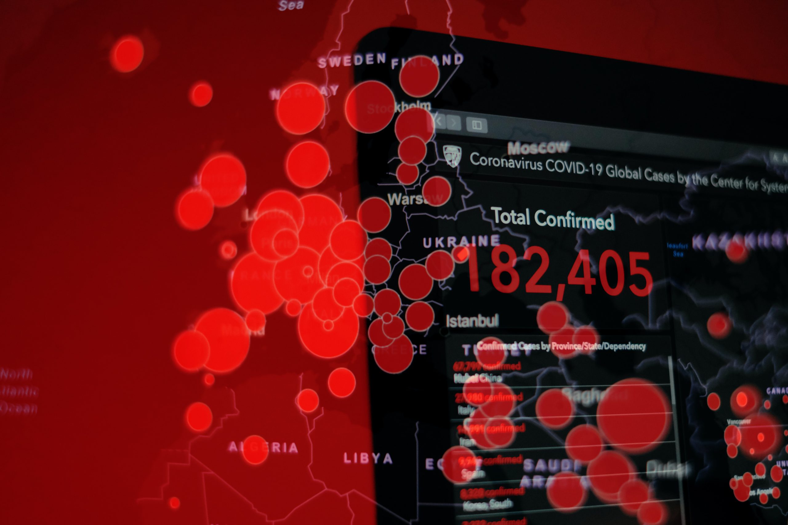 Fotografia em tons de vermelho e preto mostrando monitor de computador, que retrata focos de contágio relacionados à pandemia do COVID-19.