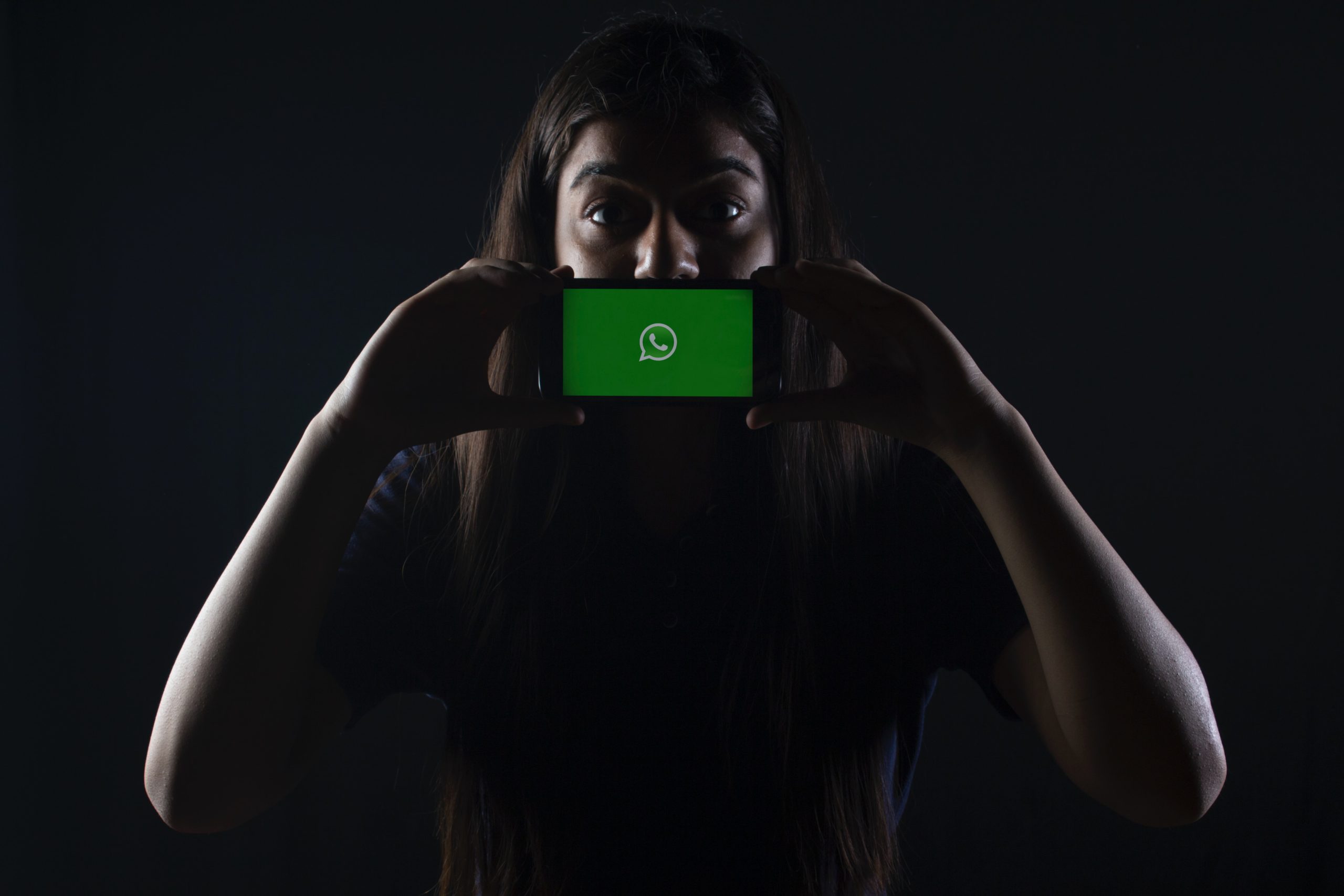 Imagem de uma mulher em um espaço escuro com celular na região da boca.